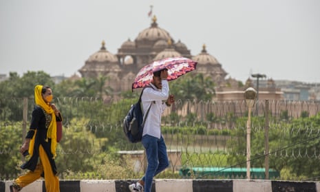 A man shelters under an umbrella as he walks past the Akshardham temple in New Delhi.