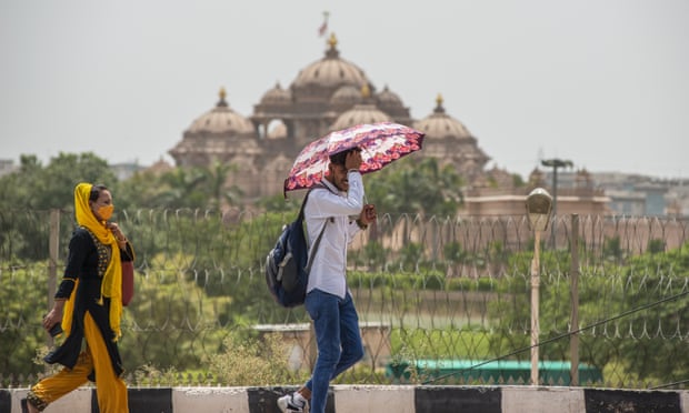 A man shelters under an umbrella as he walks past the Akshardham temple in New Delhi.