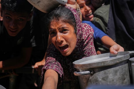 Palestinian people struggle to receive cooked food distributed at a community kitchen in the southern Gaza Strip.