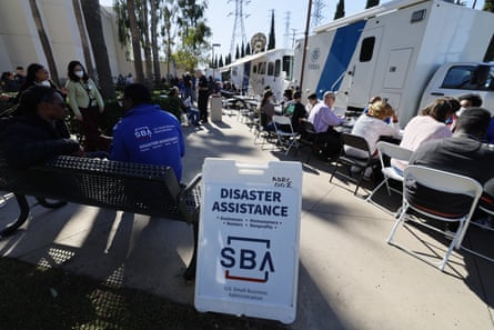 people sit in folding chairs outside next to a sign that says “disaster assistance”