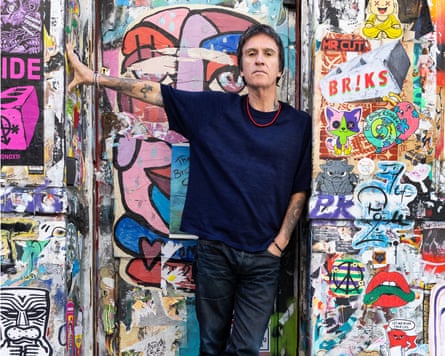A man in black standing in front of a wall full of graffiti and posters