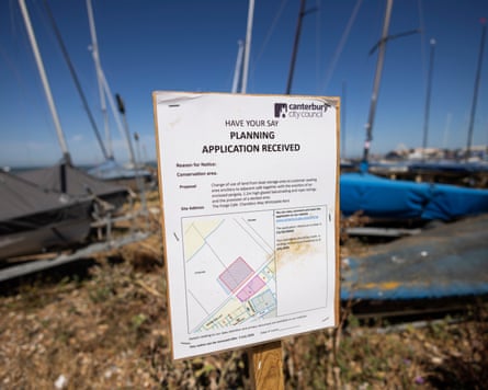 A sign for the planning application in front of boats on the beach