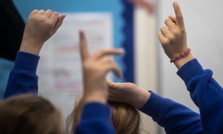 Children in blue jumpers raising their hands with their backs to the camera