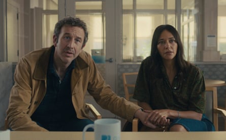 A white middled man and woman are seated and listen as if receiving news from an unseen person