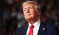 A man wearing a navy suit and red tie (Donald Trump) looks to the side while at a political rally