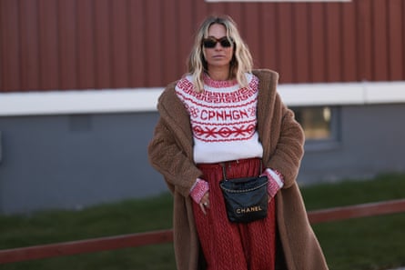 Model wearing white / red pattern knit wool pullover, brown fluffy long teddy coat, red print pattern wide pants, black leather crossbody bag
