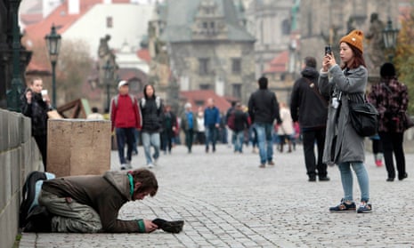 A tourist takes a picture next to a beggar on the Charles bridge in Prague.