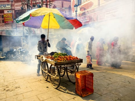 Smoky Varansi street scene with fruit seller under colourful striped umbrella