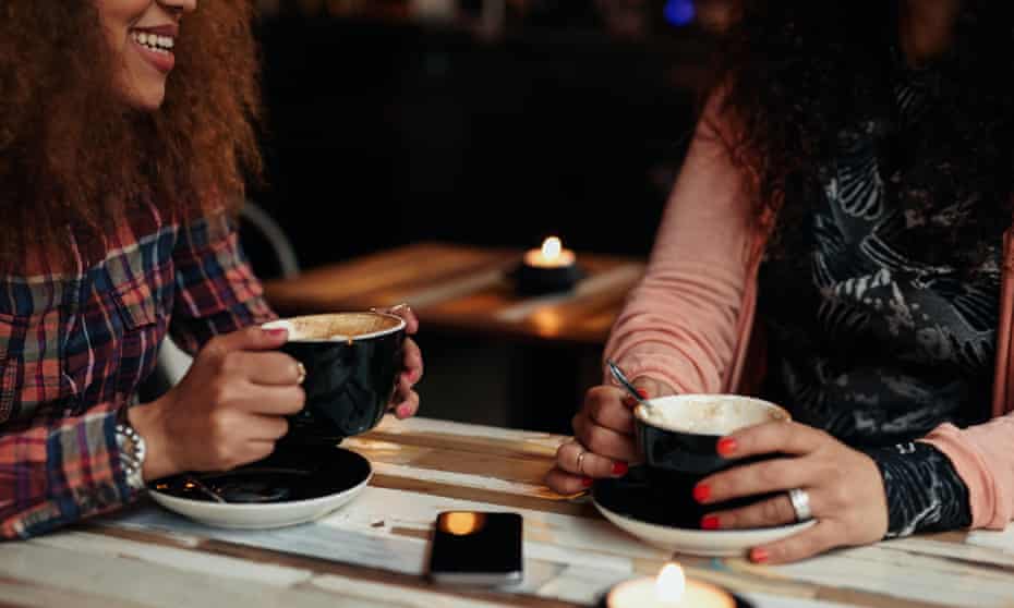Cropped shot of two women sitting at restaurant holding cup of coffee. Female friends drinking coffee at a tableF1TBE7 Cropped shot of two women sitting at restaurant holding cup of coffee. Female friends drinking coffee at a table
