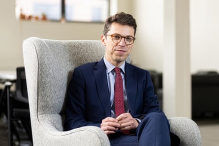 Nuno Loureiro in a navy suit with a red tie, sat in a cream armchair