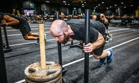 Joel Snape strains till the veins in his head show up as he tries to push a weighted sled along a black artificial track in a huge conference hall filled with other people doing similar things.