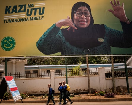 Schoolchildren walk past a billboard with an image of Hassan