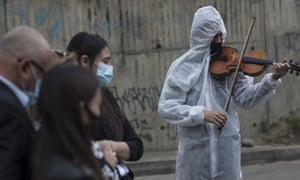 Violinist Antonio Hernandez plays for the relatives of COVID-19 victim Miryam Rodriguez, while they are gathered for prayer by the hearse that carries her remains to Serafin Cemetery, before cremation in Bogota, Colombia. Due to regulations to contain the new coronavirus, relatives cannot enter the cemetery.