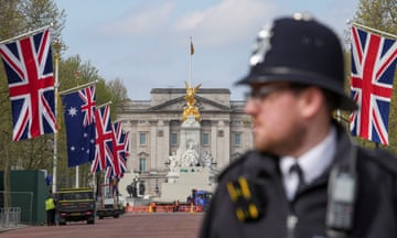 A police officer out of focus in the foreground, with Buckingham Palace behind and flags along the Mall