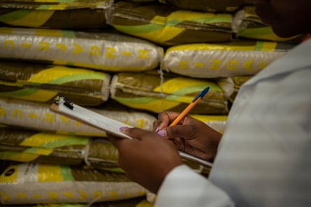 Kinuthia stands with a clipboard marking stock in front of a pile of sacks of flour.