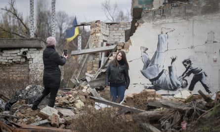 Una mujer toma una foto de otra mujer posando frente a un mural de Banksy