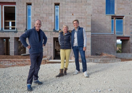 Kevin McCloud stands in front of a building being constructed, next to Piers and Emma