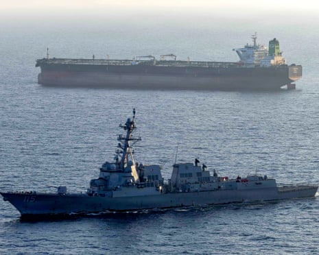A grey naval destroyer in the foreground with a large cargo tanker in the background on calm seas.