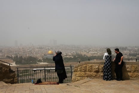 एक मुस्लिम महिला प्रार्थना कर रही है और एक यहूदी जोड़ा यरूशलेम के पुराने शहर की ओर देखने वाले जैतून के पहाड़ पर उसके बगल में खड़ा है।