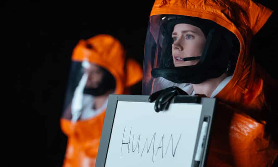 Woman in orange protective suit holds up sign saying "Human"