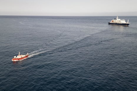 An aerial view of an ambulance boat (L) carrying crew members wearing hazmat suits as they return to port after approaching the pilot door on the starboard side of the cruise ship MV Hondius.