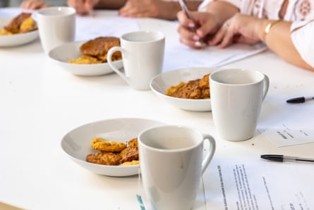Mugs of tea and plates of half-eaten Anzac biscuits on a white table. 