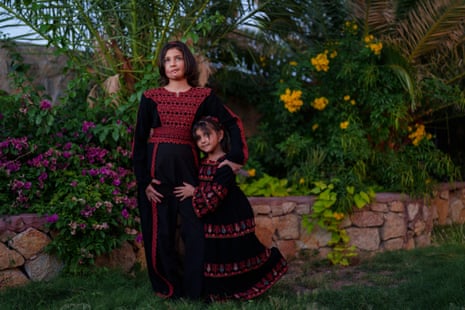Two girls dressed in traditional Palestinian black robes with elaborate red embroidery, standing together in a garden