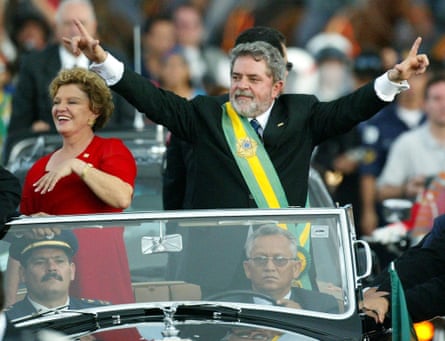 Lula standing in the back of a car that is driving through a crowd of people.