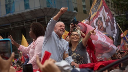 Lula with his fist in the air, standing on a car in a crowd with flags