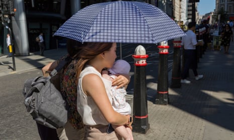 A mother carrying her child beneath an umbrella in London.