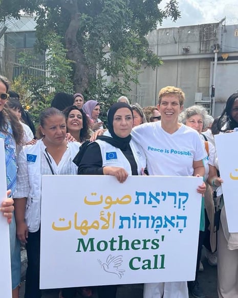 A group of women stand holding signs in Arabic, Hebrew and English which read 'Mothers' Call'.