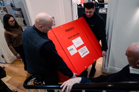 Two men carry a large wooden box through a narrow internal door