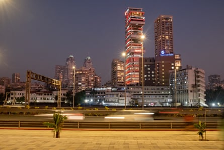 Car headlights in a blurred streak as they zip by a cityscape of tower blocks at dusk