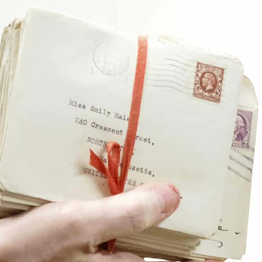 Hand holding bundle of letters tied with red ribbon, some addressed to Emily Hale with stamp with picture of the King, ones at back partly obscured, but with picture of George Washington