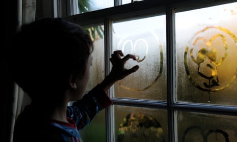 A boy drawing faces in condensation on a window. 
