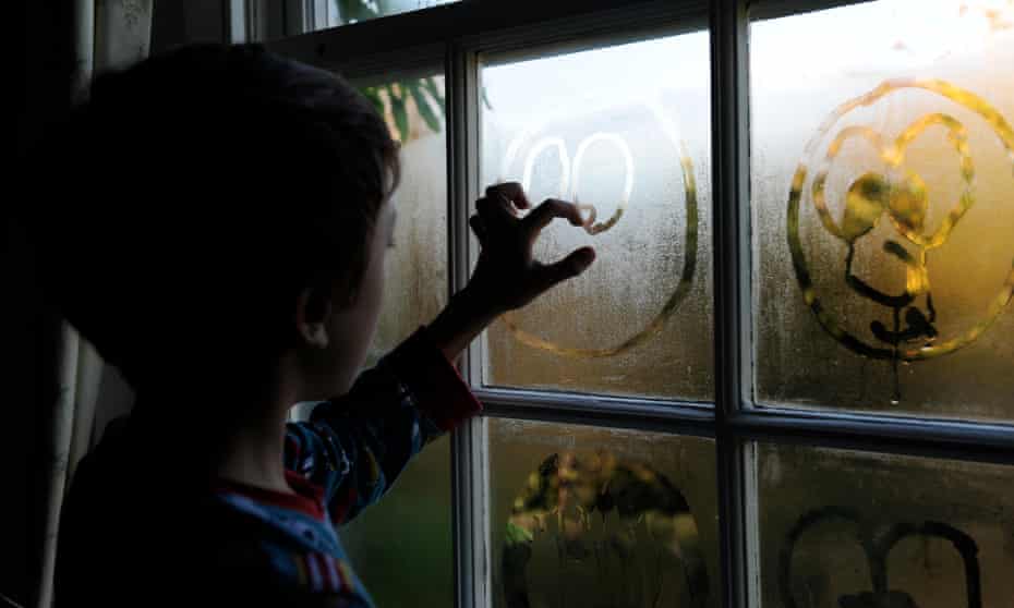 A boy draws faces in condensation on a window