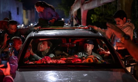 La gente rodea un coche con un hombre conduciendo a una mujer.