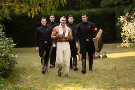 a shirt-less man walking with four men in black uniforms behind him