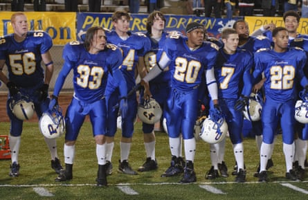 A group of teenagers in a royal blue team kit stand on the football pitch, holding their protective headwear