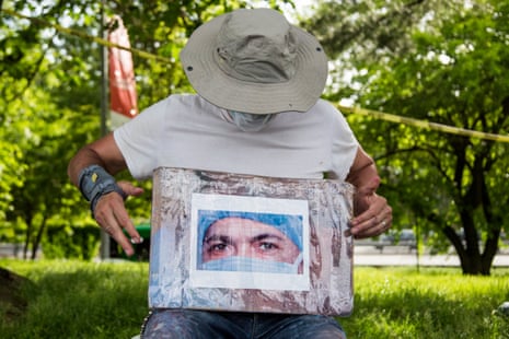 Artist Jorge Rodríguez holds up a photo of Dr. Ydelfonso Decoo while painting a mural in Queens, New York. Dr. Ydelfonso Decoo, an immigrant doctor, died of complications from Coronavirus.