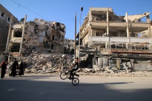A boy rides a bicycle past damaged buildings in the rebel-held Seif al-Dawla neighbourhood