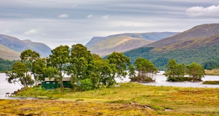 A green building among trees, with lake and mountains behind