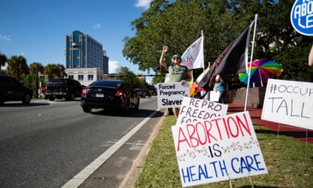 A small crowd holding signs and waving as cars pass by the Leon County courthouse in Tallahassee, Florida