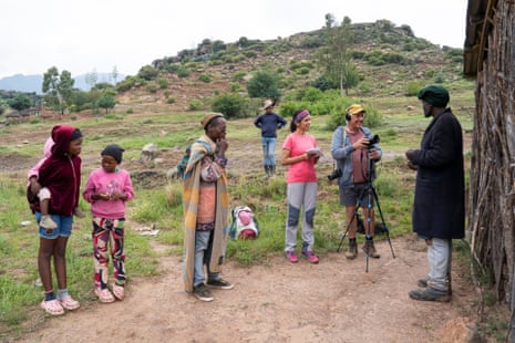 Sheena Shah and Matthias Brenzinger record Tsotleho Mohale standing outside a wooden house in a grassy clearing with four more people nearby