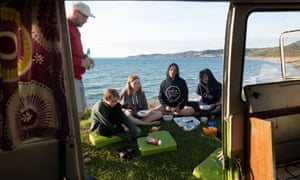 Family picnicking by van with sea in background