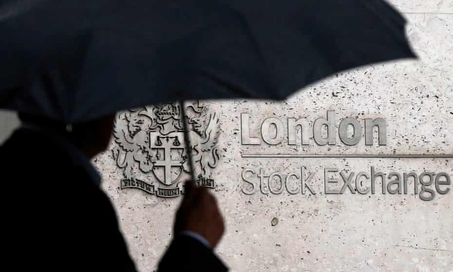 A man shelters under an umbrella as he walks past the London Stock Exchange