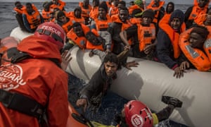 Aid workers rescue migrants aboard an overcrowded rubber boat 60 miles north of the Libyan coast.