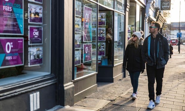 A couple walk past an estate agent in London