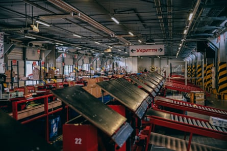 A large industrial unit with rows of sorting machines in it. Along one wall are shelves with packages on them