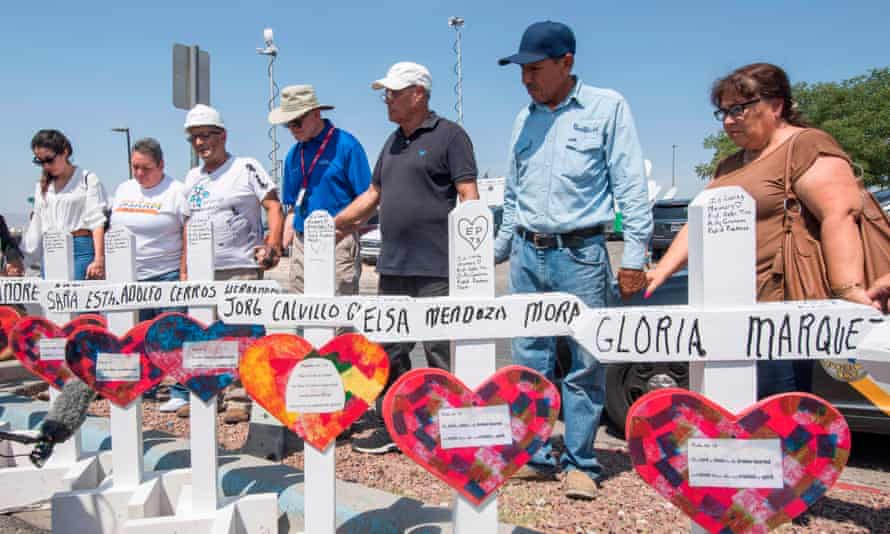 People pray beside crosses with the names of victims who died in the El Paso shooting.